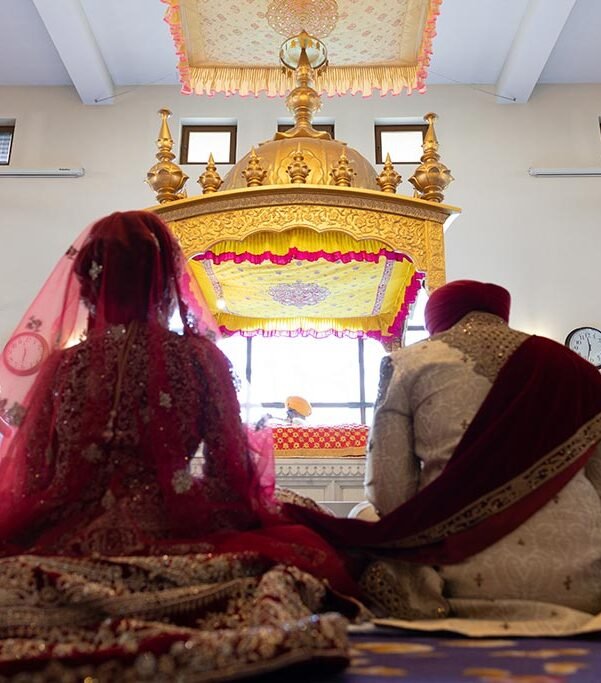 Bride and groom seated before Guru Granth Sahib Ji during the Anand Karaj ceremony photographed by a Sikh Wedding Photographer in London